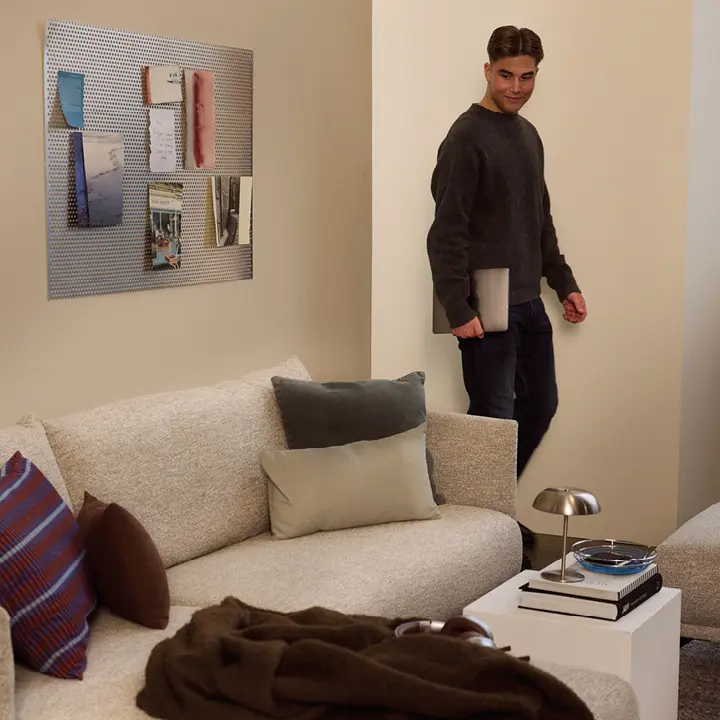Helles Sofa mit Kissen, Beistelltisch und Lampe, Person mit Laptop im Hintergrund